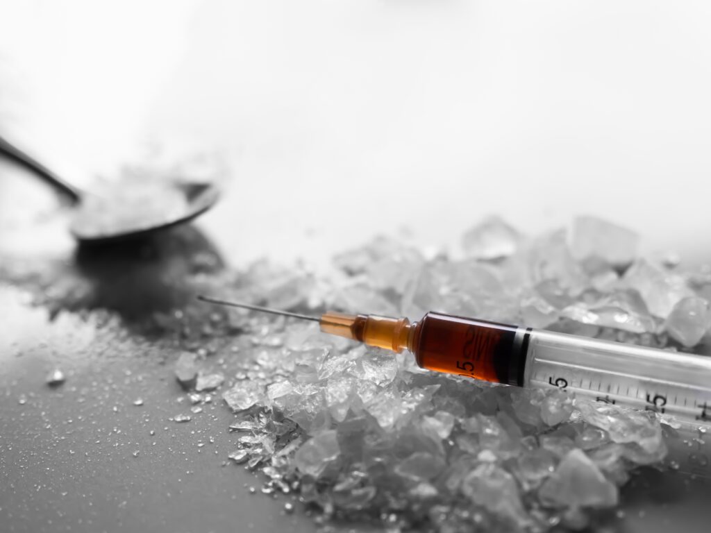 A spoon filled with crystal meth that is spilled out on to a table with a syringe represents the dangers of using and snorting meth.