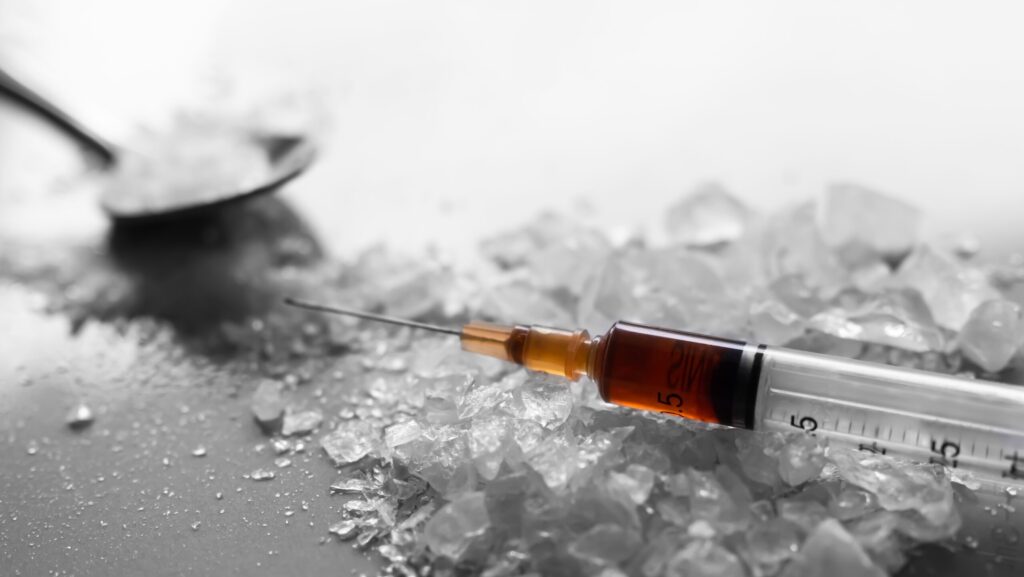 A spoon filled with crystal meth that is spilled out on to a table with a syringe represents the dangers of using and snorting meth.