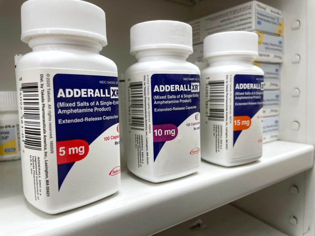 Bottles of Adderall in varying strengths on a pharmacy shelf representing methamphetamine vs Adderall.