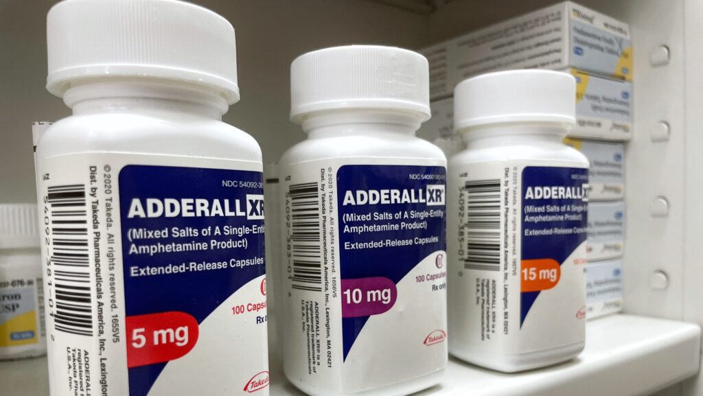 Bottles of Adderall in varying strengths on a pharmacy shelf representing methamphetamine vs Adderall.