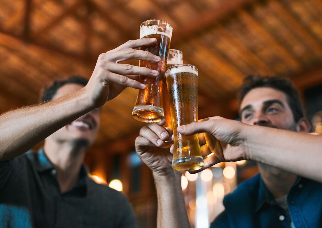 A group of young men holding up tall glasses of beers and unaware of the relationship between alcohol and prostate cancer.