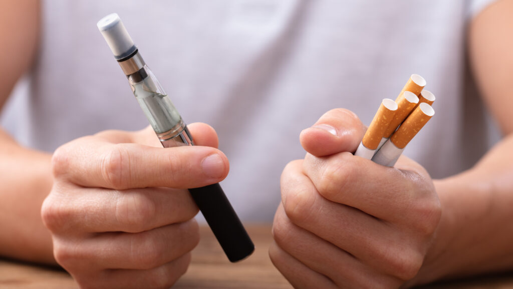 A man hold a vape in in one hand and cigarettes in the other wonders how long it takes to get addicted to nicotine.