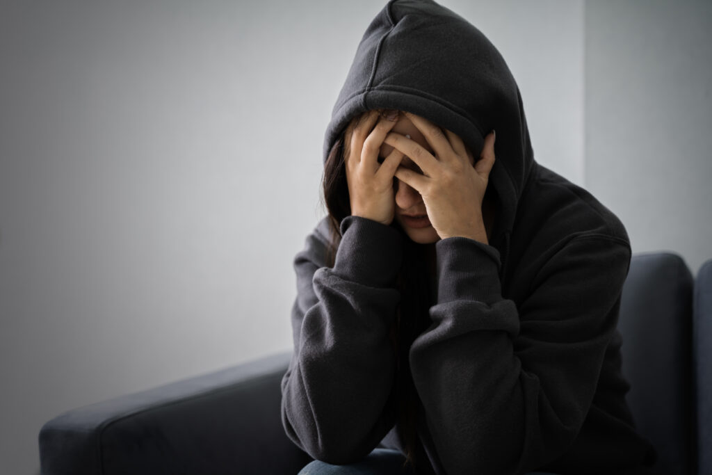 A young woman wearing her hood over her hand and hands on her face is suffering from a xanax hangover.