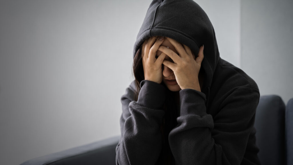 A young woman wearing her hood over her hand and hands on her face is suffering from a xanax hangover.