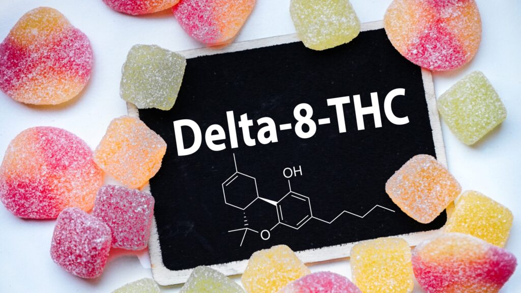 The words Delta 8 THC on a black board is surrounded by various types of gummies represents how long Delta 8 stays in your system.